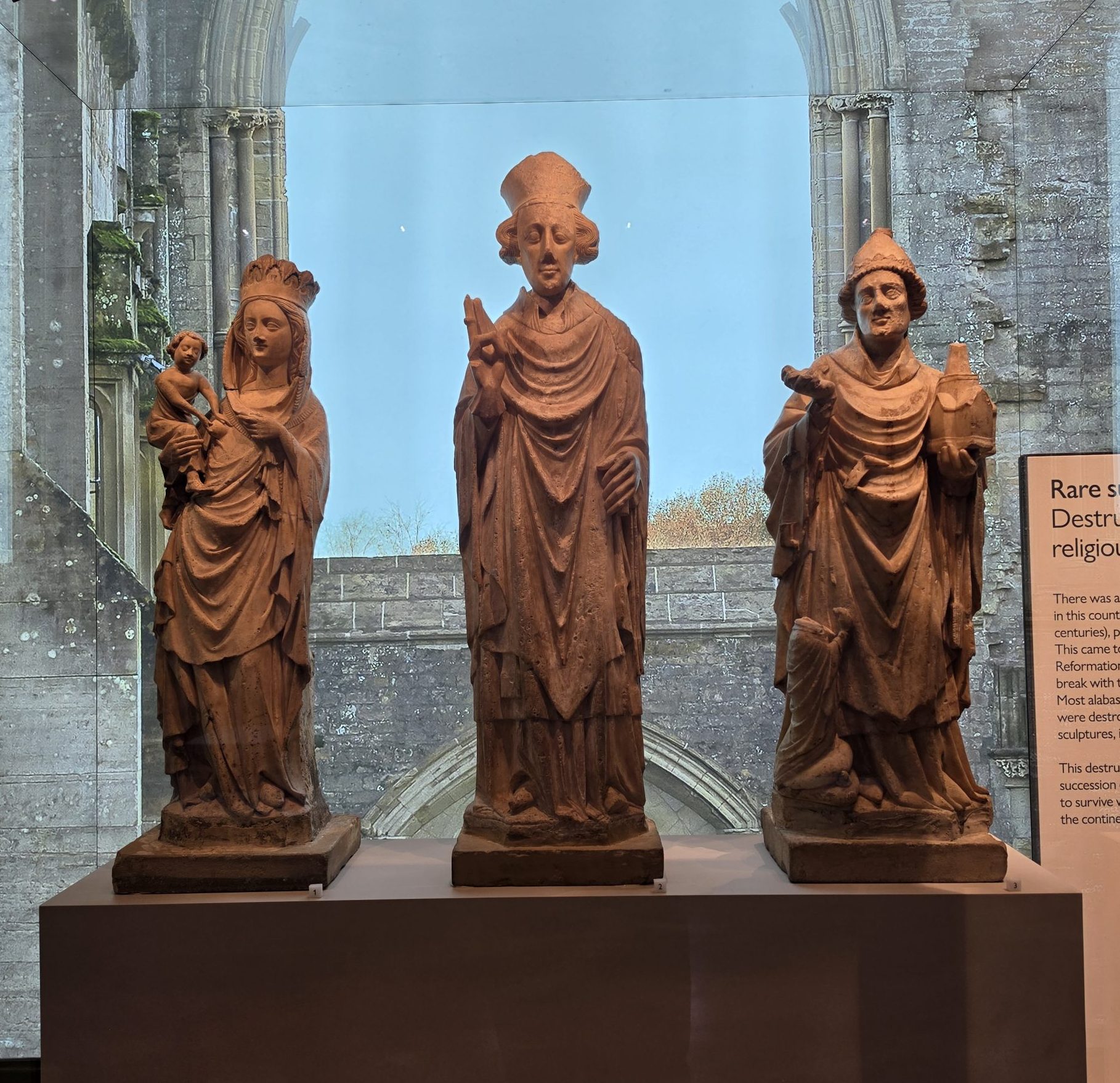 Three alabaster figures in museum setting. Virgin and Child, a bishop, St Peter as Pope.